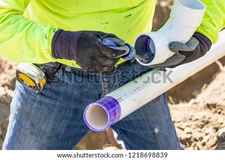 Plumber Applying Pipe Cleaner, Primer and Glue to PVC Pipe At Construction Site.