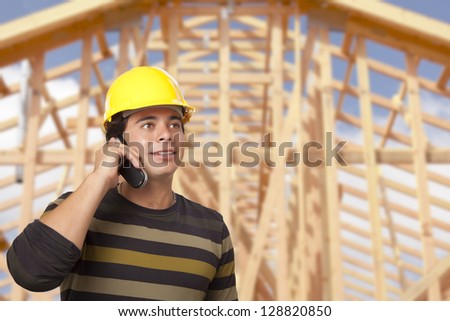 Handsome Hispanic Male Contractor on Phone in Front of New House Framing.