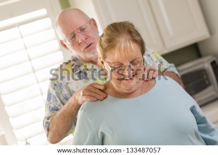 Happy Senior Adult Husband Giving Wife a Shoulder Rub in the Kitchen.