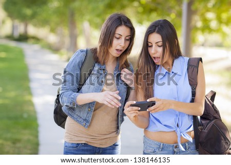 Young Adult Mixed Race Twin Sisters Sharing Cell Phone Experience Outside.