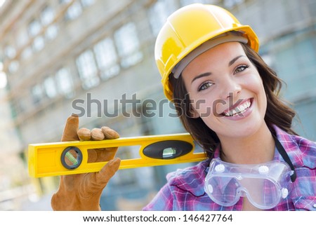 Portrait of Young Attractive Female Construction Worker with Level Wearing Gloves, Hard Hat and Protective Goggles at Construction Site.