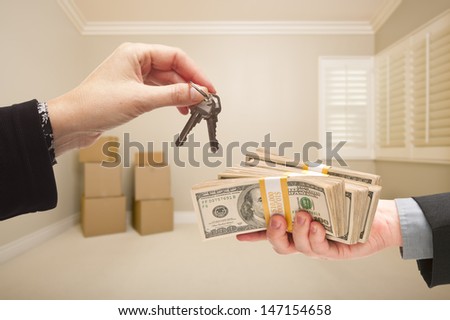 Man and Woman Handing Over Cash For House Keys Inside Empty Tan Room with Boxes.