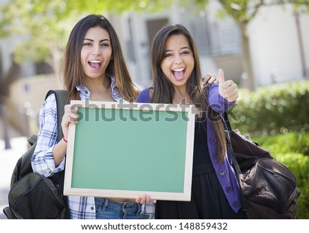 Portrait of Two Attractive Mixed Race Female Students Holding Blank Chalkboard with Thumbs Up and Carrying Backpacks on School Campus.