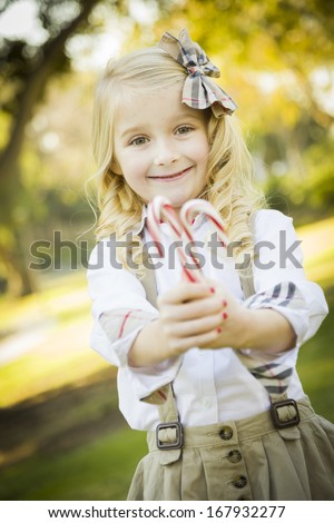 Cute Little Girl with a Bow in Her Hair Holding Her Christmas Candy Canes Outdoors.