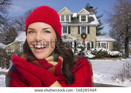 Smiling Mixed Race Woman in Winter Clothing Outside of Decorated House in the Snow.