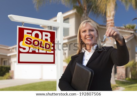 Female Real Estate Agent Handing Over the House Keys in Front of a Beautiful New Home and Real Estate Sign.