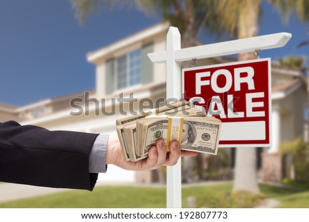 Buyer Handing Over Cash for House with Home and For Sale Real Estate Sign Behind.