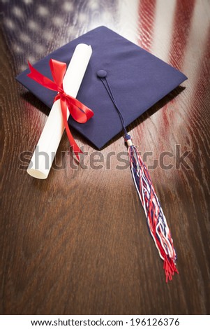 Graduation Cap with Tassel and Diploma Wresting on Wooden Table with American Flag Reflection.