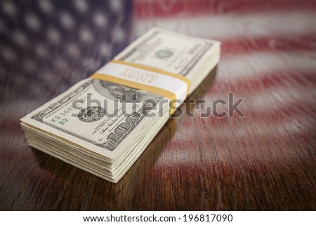 Thousands of Dollars Stacked with Reflection of American Flag on Wooden Table.