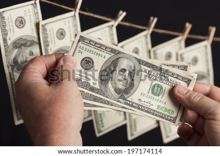 Male Hands Holding Hundred Dollar Bills with Several Hanging From a Clothesline on a Dark Background.