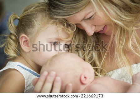 Beautiful Young Mother Holds Newborn Baby Girl as Young Sister Looks On.