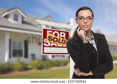 Attractive Mixed Race Woman in Front of House and Sold Real Estate Sign.