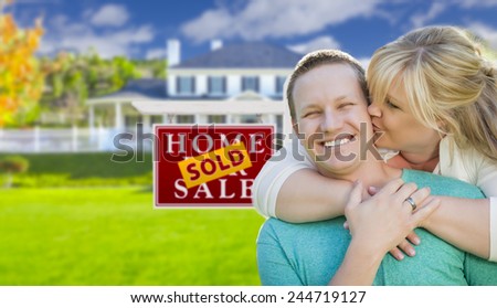 Happy Couple Hug In Front of Sold Real Estate Sign and Beautiful New House