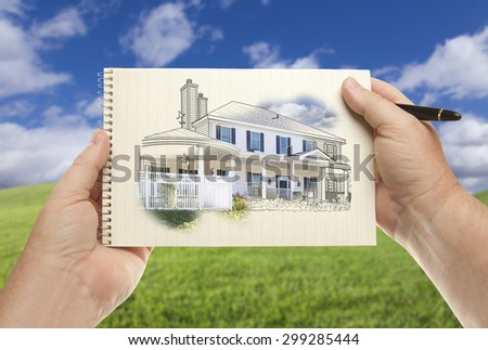 Male Hands Holding Pen and Pad of Paper With House Drawing Over Empty Grass Field and Sky.