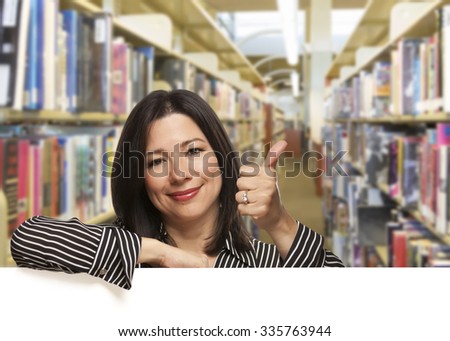 Pretty Hispanic Woman with Thumbs Up Leaning On White Board in the Library.