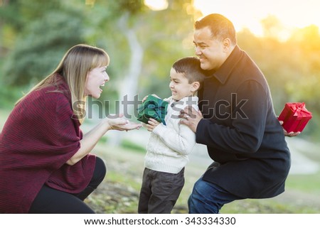 Happy Young Mixed Race Son Handing Gift to His Mom As Father Stands Behind.