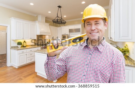 Smiling Contractor with Level Wearing Hard Hat Standing In Custom Kitchen.