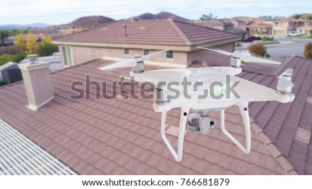 Unmanned Aircraft System (UAV) Quadcopter Drone In The Air Over House Inspecting the Roof.
