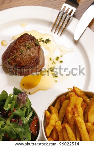 Meat food : roast steak boneless served with green lettuce salad and golden French fries potatoes on dish with fork and knife
