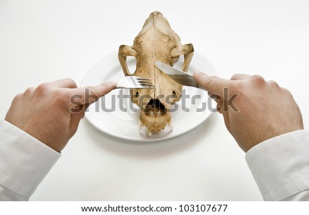 Famine concept. Man eat animal skull with fork and knife.