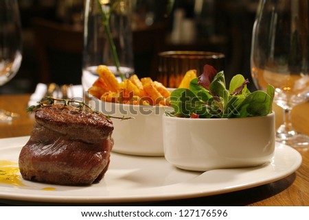 roast steak served with green lettuce salad and golden French fries potatoes on dish.