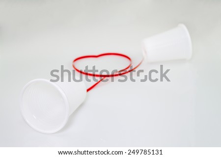 Long distance relationship concept. 2 white plastic cups connected with a red thread