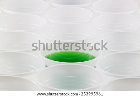 Lots of white plastic cups. One cup filled with green water. Shallow depth of field.