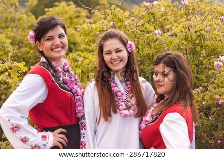 Women dressed in a Bulgarian traditional folklore costume picking roses in a garden, as part of the summer regional ritual in Rose valley, Bulgaria.