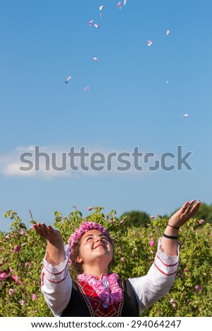 Woman dressed in a Bulgarian traditional folklore costume picking roses in a garden, as part of the summer regional ritual in Rose valley, Bulgaria.