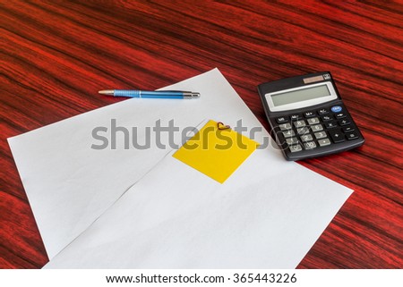Heart shaped paper clip attached to a sheet of paper with a yellow sticky note. Calculator and pen laying aside