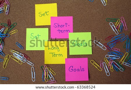 Set long term and short term goals written on post it notes on bulletin board with colorful paperclips