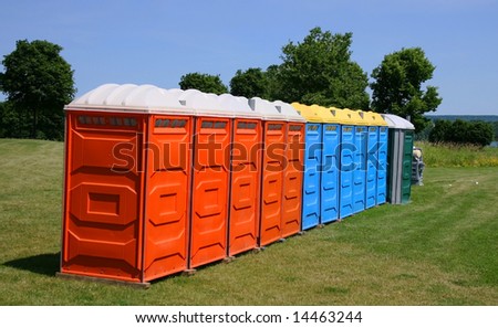 Several colorful outdoor toilets lined up ready for an outdoor event.