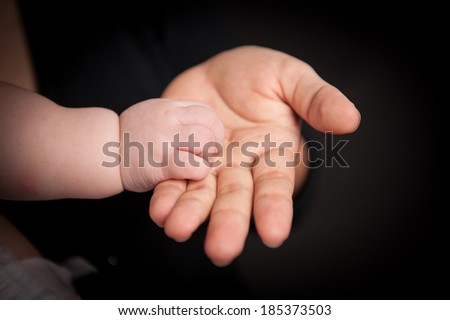 mother holding baby hand, black background