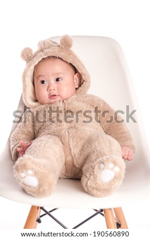 Adorable baby boy wearing a teddy bear suit sitting on chair