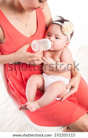 Young mother feeding her new baby girl with a milk bottle. Isolated on white background