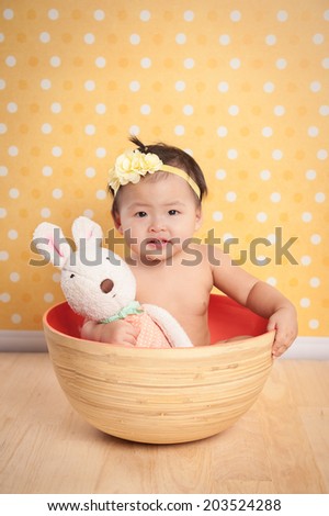 Adorable infant wearing a crochet hat and sitting in a pot, isolated on yellow background