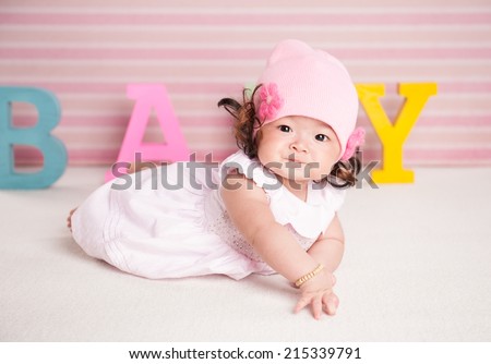 Portrait of a crawling pretty baby with pink hat on the bed in her room. text concept