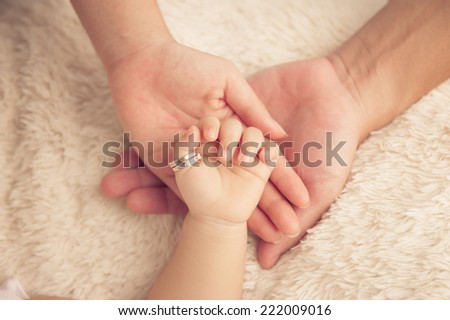 Baby hand. Closeup of baby hand into parents hands. Family concept with the wedding rings in baby finger.