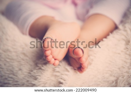 Baby feet on white blanket with the wedding rings in baby toe