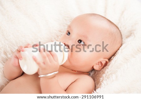 Beautiful little baby with a milk bottle under a warm knitted blanket