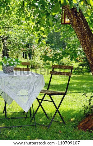 Idyllic setting of a small coffee table and a wooden chair under an apple tree in green summer garden