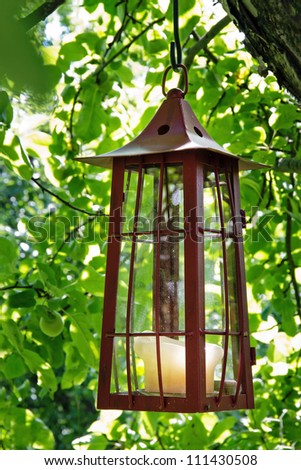 Picturesque old rustic candle lantern hanging in an apple tree in green summer background