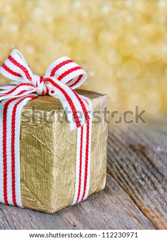 Golden Christmas gift box with a red ribbon and bokeh background