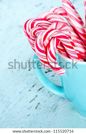 Striped Christmas candy canes in a light blue / turquoise cup with shabby chic wooden background