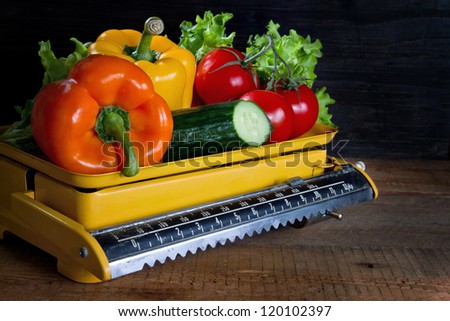 Fresh vegetables on a scale, with rustic wooden and black background, weight loss concept