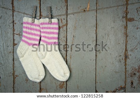 Two white woolen socks with pink stripes hanging from clothespins in front of wooden rustic background