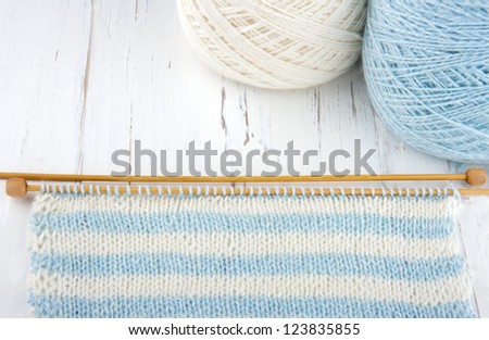 Knitting on white wooden background, light blue and white stripes