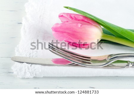 Closeup of pink tulip at rustic dinner setting, on white wooden table