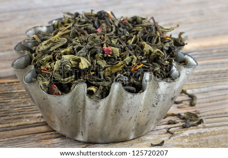 Loose green tea leaves in a rustic metal cupcake on wooden background