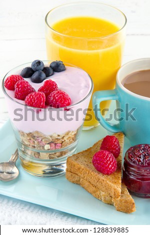 Healthy breakfast with yoghurt, berries, juice, toast and coffee, on white wooden background